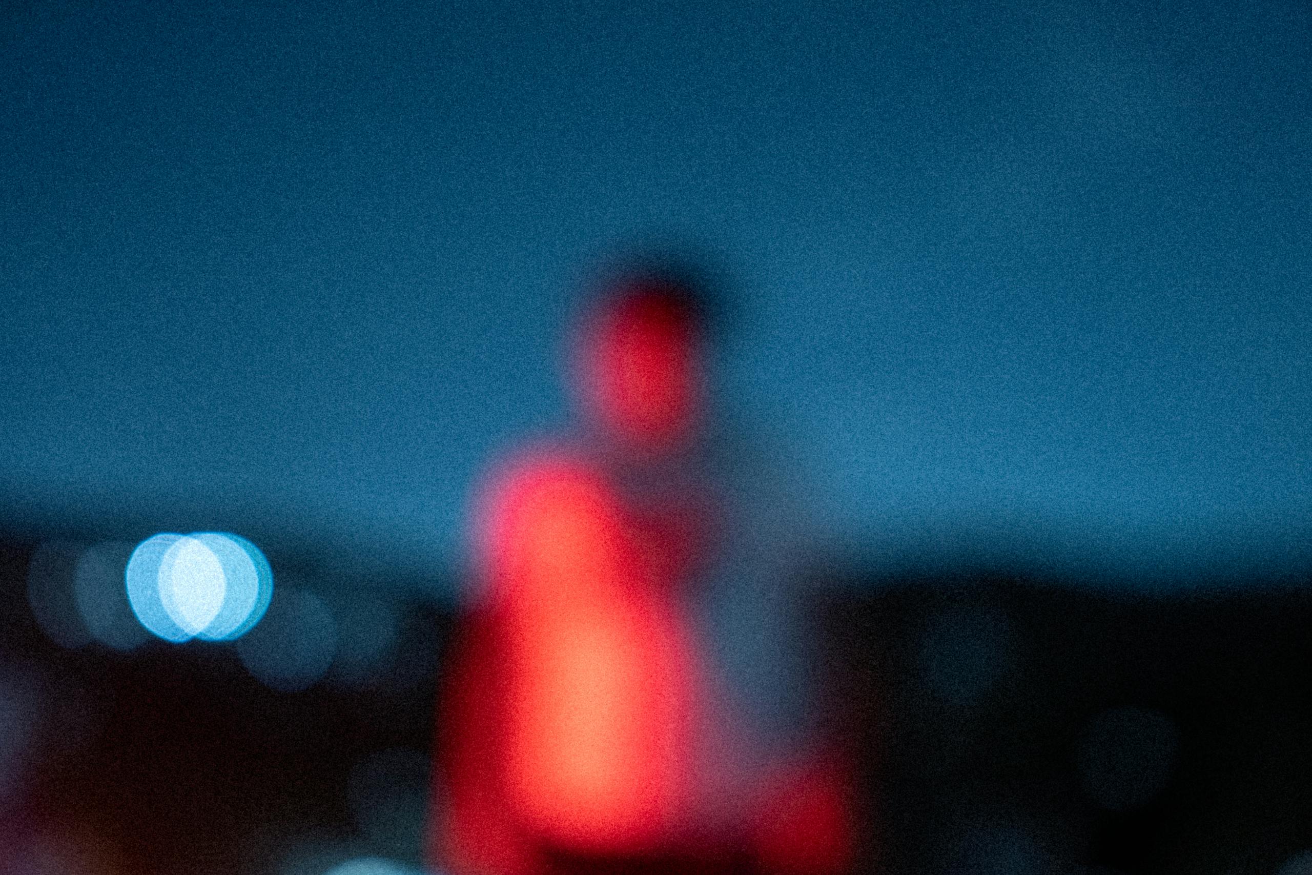 A creative and blurry portrait of a person at night, illuminated by red light against a deep blue background.