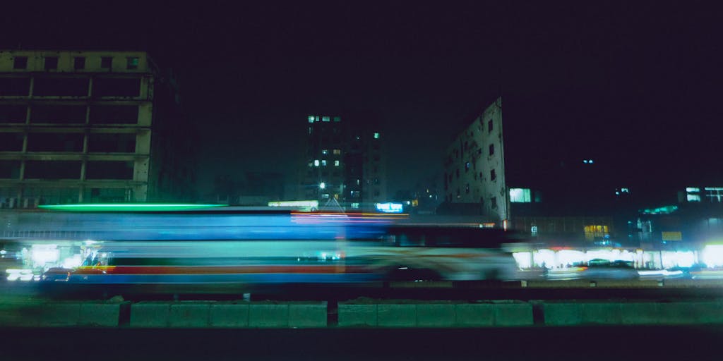 A vibrant nighttime scene in Dhaka with blurred traffic lights and urban architecture.